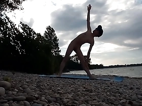 A skinny naturist young man performs yoga outdoors at a beach.