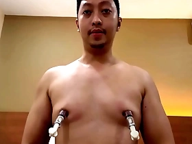 Young and Asian man with a naked body uses nipple pumps to enhance his pleasure.