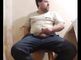 A chubby gay man sits down on a chair to pleasure himself.